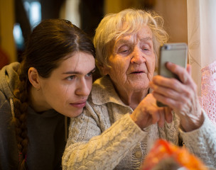 Wall Mural - An elderly woman looks at a smartphone, with his adult granddaughter.