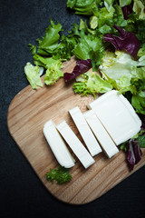 Wall Mural - Greek feta cheese on a wooden board, lettuce leaves on a black background.