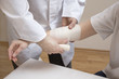 Dłonie lekarza zakładają opatrunek z bandaża na przedramie kobiety