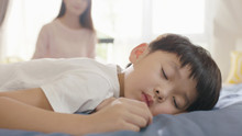 Asian Boy Sleeping In Bed In The Morning While Mother Sitting In Background