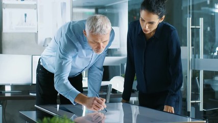 Poster - Senior Male and Young Female Architectural Designers Draw Building Concept on a Graphics Tablet Display Vertical Touchscreen Table. They Use Gestures for Zooming Project Model. 