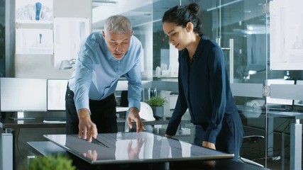 Poster - Senior Male and Young Female Architectural Designers Draw Building Concept on a Graphics Tablet Display Vertical Touchscreen Table. They Use Gestures for Zooming Project Model. 