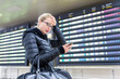 Stressed worried woman in international airport looking at smart phone app information and flight information board, checking her flight detailes.