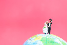 Miniature People Bride And Groom On The Globe With Pink Background , Valentine's Day Concept