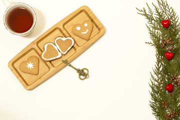 Wall Mural - Valentines day concept: Cookies in heart shape symbolize Love decorated with glass of tea, old golden key and green pine branches isolated on white background. Top view. Macro, close up.