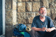 © Srdjan - Homeless man, Happy and smiling poor homeless man sitting in the shadow of the building on the urban street in the city