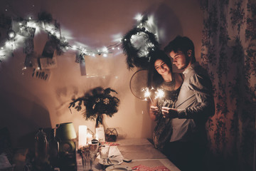 Wall Mural - happy new year and merry christmas concept. happy stylish hipster couple holding burning sparklers fireworks and embracing in room at hoome in evening. happy holidays. toned