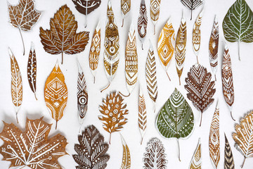 A lot of autumn dry leaves with white hand-drawn ethnic patterns.