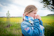 Little girl blowing her nose suffering from pollen allergy outdoor by a field