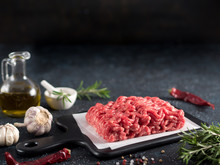 Fresh Raw Minced Beef On Backing Paper And Cutting Board And Ingredients Over Black Cement Background With Copy Space.