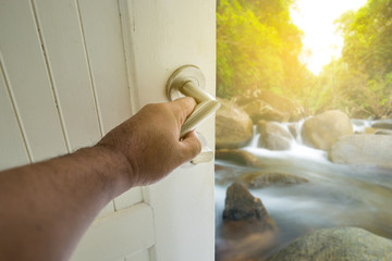 Wall Mural - hand on white door open to waterfall with sun light