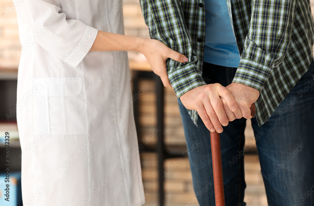 Senior man with walking stick and young caregiver, indoors