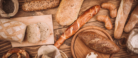 Many mixed baked breads and rolls on rustic wooden table