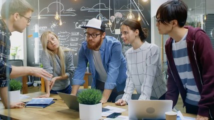 Poster - Team Leader Shows Laptop to a Group of Talented Young Developers, They Start Discussion at the Meeting Table. Creative People in Stylish Office Environment. Shot on RED EPIC-W 8K Helium Cinema Camera.