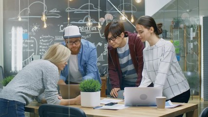 Poster - Team Meeting of Developers, They Lean on the Table and Look at the Results Shown on the Laptop. Creative Young People in Stylish Office Environment. Shot on RED EPIC-W 8K Helium Cinema Camera.