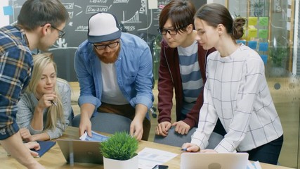 Poster - Team Meeting of Developers, They Lean on the Table and Look at the Results Shown on the Laptop. Creative Young People in Stylish Office Environment.Shot on RED EPIC-W 8K Helium Cinema Camera.