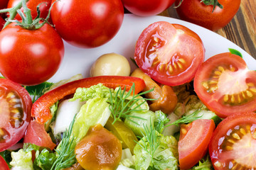 Salad with tomatoes, cabbage, pickled mushrooms and sweet red pepper. In a white dish close up.