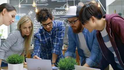 Poster - Team Meeting of Developers, They Lean on the Table and Look at the Results Shown on the Laptop. Creative Young People in Stylish Office Environment. Shot on RED EPIC-W 8K Helium Cinema Camera.