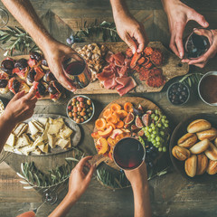 Wall Mural - Flat-lay of friends hands eating and drinking together. Top view of people having party, celebrating together at vintage wooden rustic table set with different wine snacks and fingerfoods, square crop