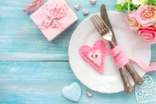 Romantic Dinner Concept. Table Place Setting With A White Plate, Vintage Silverware Tied With A Pink Ribbon And Many Different Heart Shape Decorations, A Gift And Flowers