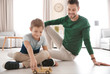 Cute little boy and father playing with toy car on floor at home