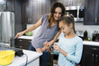 © Inti St. Clair - Mom looking at something on daughter's smart phone while cooking