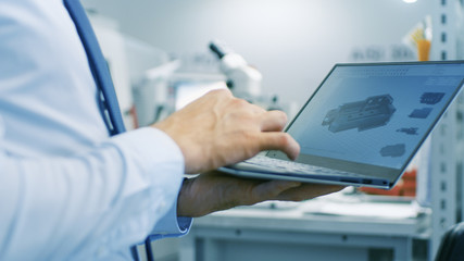 Wall Mural - Close-up of the Engineer Holding Laptop with CAD Component Model on Screen. In the Background Modern Factory Equipment.