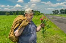 Senior Man With Sack And Bunch Of Wild Flowers Standing On A Roadside In Central Ukraine