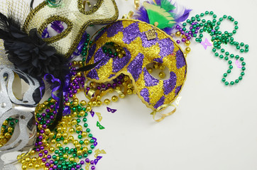 Mardi Gras border or frame of carnival masks, beads, ribbons and confetti in purple, green, gold and black on light background. Copy space