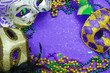 canvas print picture - Mardi Gras border or frame of carnival masks, beads, ribbons and confetti in purple, green, gold and black on background of rough textured sparkly paper