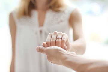 Wall Mural - Man holding fiancee's hand with engagement ring on blurred background
