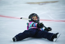 A Five Year Old Girl In Hockey Equipment And Skates Falling Down On The Ice At A Skating Rink