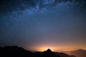 The wonderful starry sky on Christmas time and the majestic high mountain range of the Italian Alps, with glowing villages below.