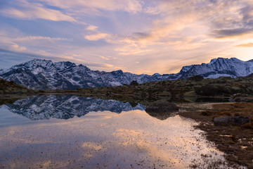 Wall Mural - High altitude alpine lake in idyllic landscape. Reflection of snowcapped mountain range and scenic colorful sky at sunset. Wide angle shot taken on the Italian Alps.