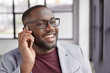 © WHstudio Leushin N - Photo of cheerful black male with shing smile, has white perfect teeth, calls secretary, dressed formally, stands in spacious cabinet. Handsome African American male financier has phone conversation