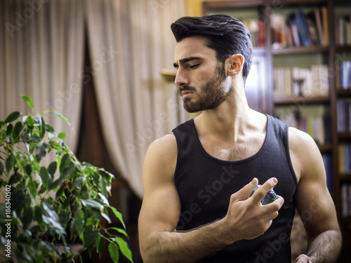Fotomural Handsome muscular young man in his home spraying cologne or perfume on neck
