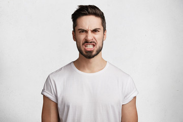 Wall Mural - Irritated grumpy fashionable young man has displeased expression, clenches teeth in anger, expresses negativity, being discontent with bad results of somebody`s work, has quarrel with somebody.