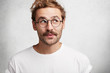 © WHstudio Leushin N - Photo of pleased dreamy male wonk with trendy hairdo, wears spectacles and casual white t shirt, imagines something pleasant, looks upwards with intriguing expression, isolated on concrete wall