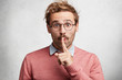 © wayhome.studio - Portrait of silent male looks with shocking expression, makes hush gesture, being stupefied, demands complete quiet atmosphere, isolated over white concrete background. Shh sign. Keeping secrecy