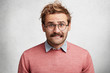 © wayhome.studio - Portrait of nervous hipster guy bites lips, has displeased expresion, trendy hairdo and mustache, worries before important meeting, isolated over white concrete background. Human reaction concept