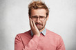 © WHstudio Leushin N - Sorrorful bearded stylish guy has toothache, keeps hand on cheek, looks with desperate misreable expression, isolated over white concrete background. Handsome frustrated sad man feels sorry.