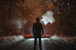The man smoke on the snowy road in the forest. evening night time