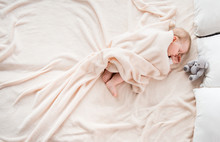 Top View Of Little Baby Covered With Blanket Sleeping On Soft Bed. She Is Suckling Her Thumb. Copy Space In Left Side