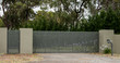 Metal driveway entrance gates set in brick fence leading to rural property with eucalyptus trees in background