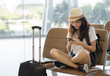 Asian woman teenager using smartphone at airport terminal sitting with luggage suitcase and backpack for travel in vacation summer relaxing waiting flight transport