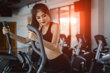 Wall Mural - Asian woman Exercise Elliptical cardio running workout at fitness gym taking weight loss with machine aerobic for slim and firm healthy lifestyle in the morning.