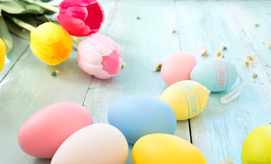 Wall Mural - Colorful Easter eggs with tulip flower on rustic wooden planks background. Holiday in spring season. vintage pastel color tone. Close-up composition.