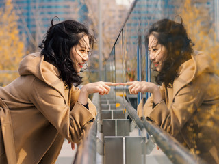 Beautiful Chinese girl looking at her mirror image in glass.