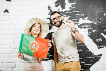 Wall Mural - Couple of young travelers standing with portuguese flag near the wall with world map, dreaming about summer vacations in Portugal