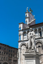 Famous Statue Of Francesco Burlamacchi And The Church Of San Michele In Foro In The City Center Of Lucca, Italy. Historic Place With Beautiful Cathedral And Archangel.